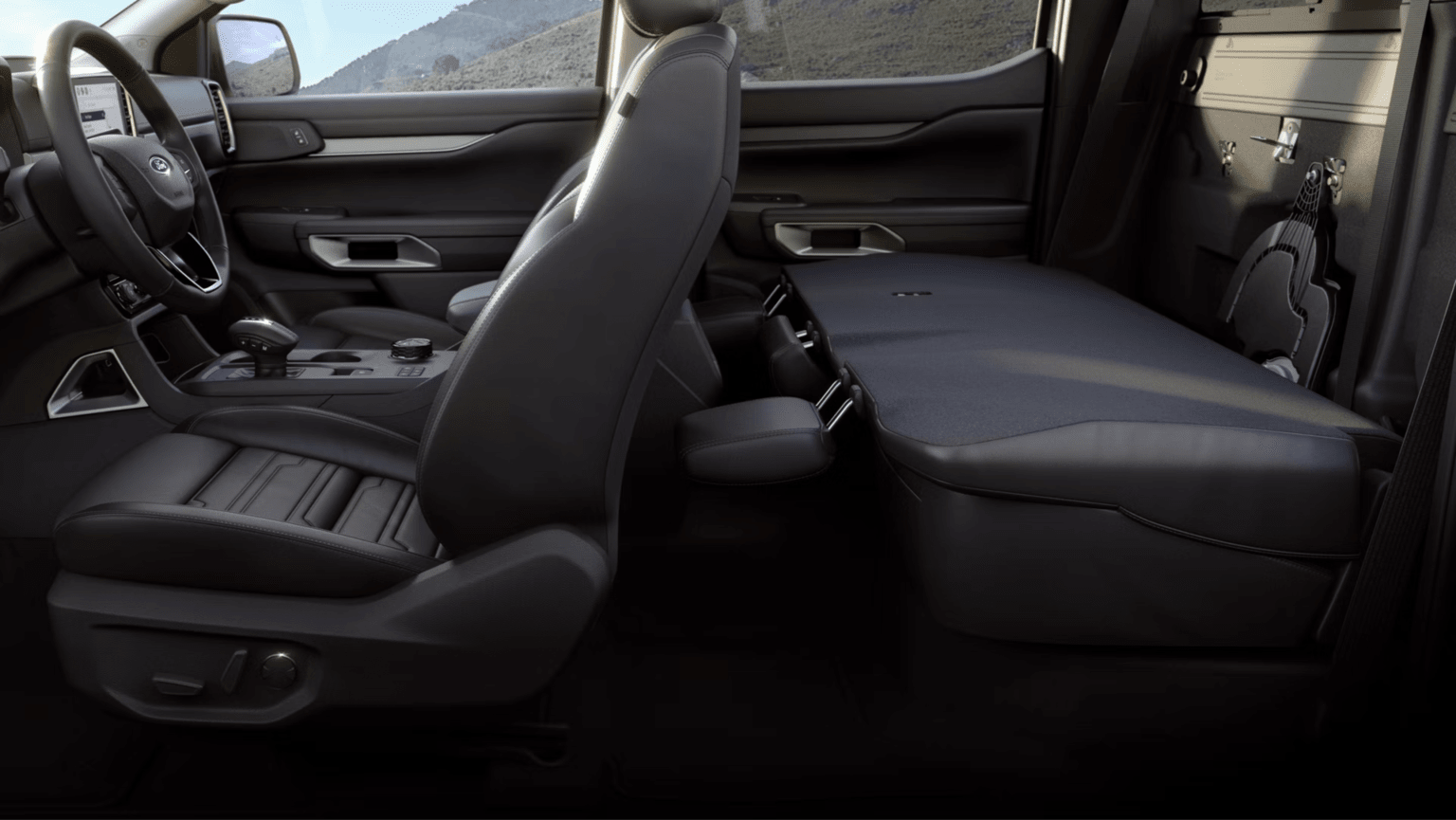 Image of a truck's dark leather interior with driver's seat and folded-down rear seat, with a blurred mountainous landscape in the background.