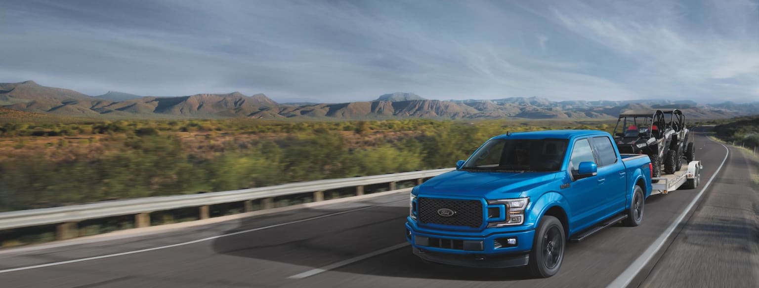 a blue truck driving down a highway with mountains in the background and a blue truck with a trailer behind it