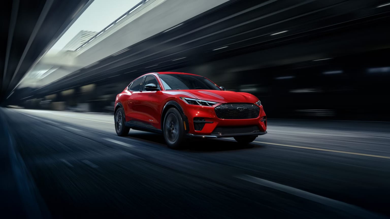 A red electric SUV driving on a dark road under a blurry concrete overpass.