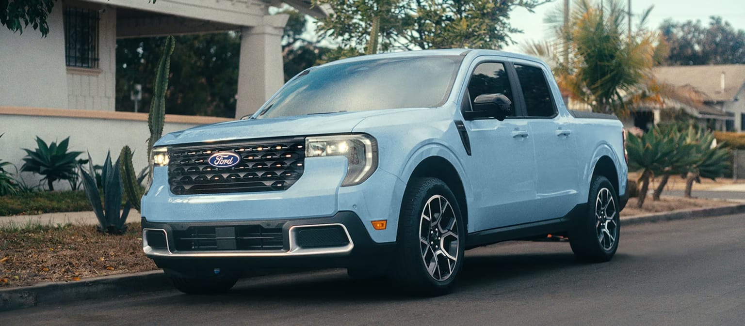 A white pickup truck with a rugged, off-road design parked in front of a residential building surrounded by lush greenery.