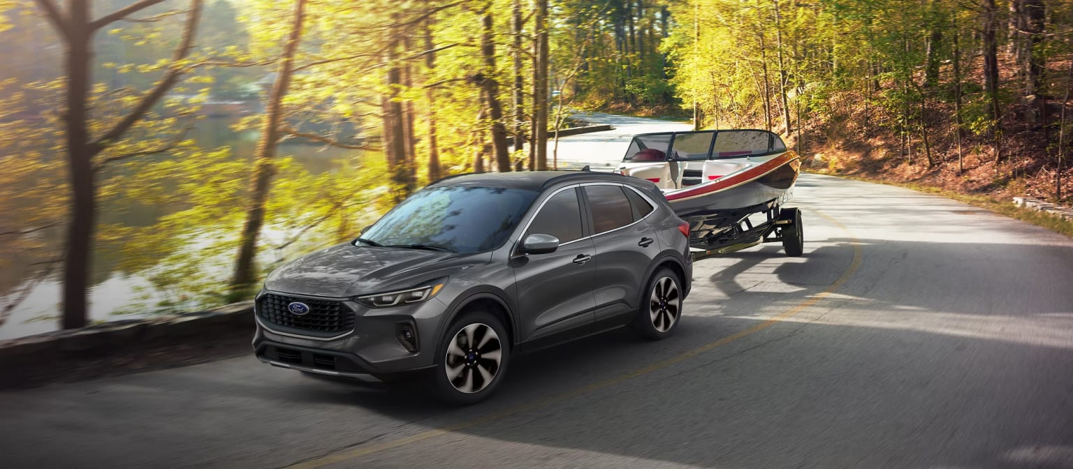 A gray SUV driving down a winding road surrounded by a lush, autumnal forest with vibrant yellow and orange foliage.