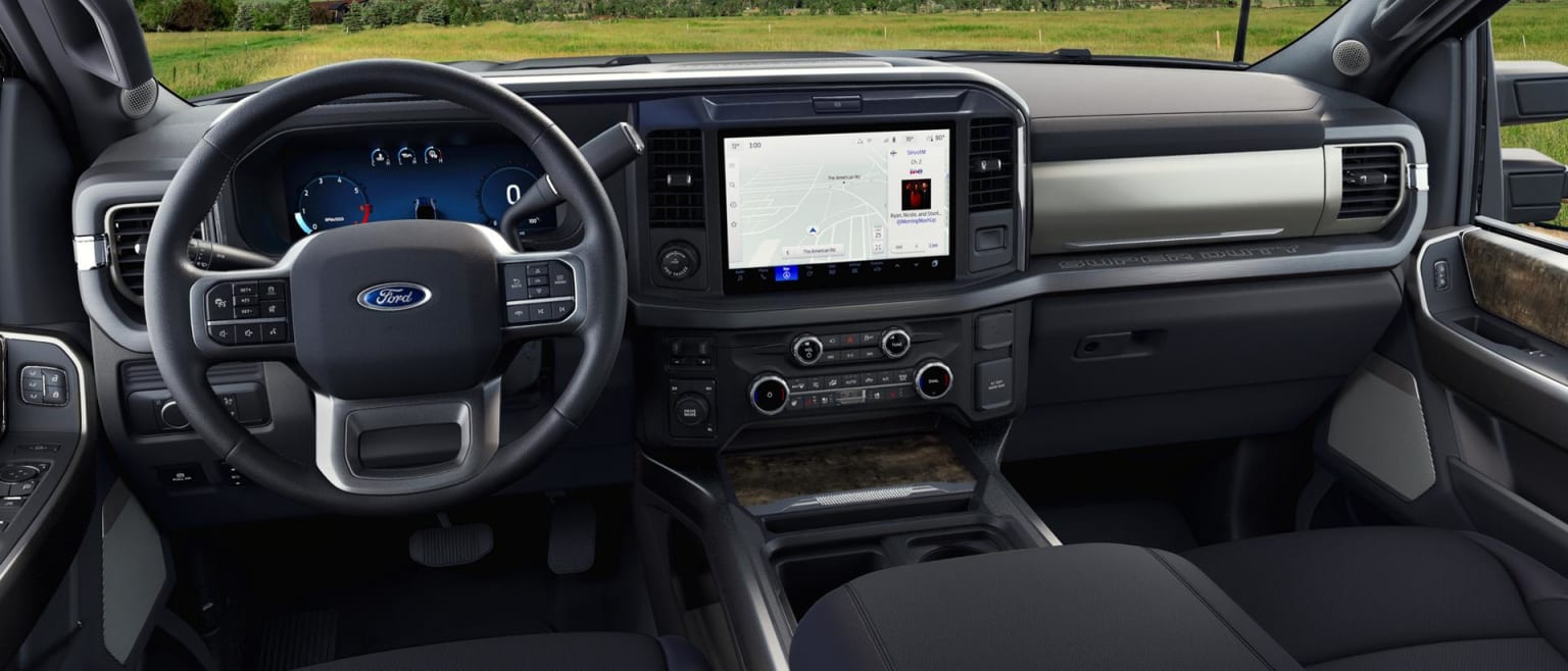 The image shows the interior of a vehicle, with a dashboard featuring a large touchscreen display, various controls, and a steering wheel.