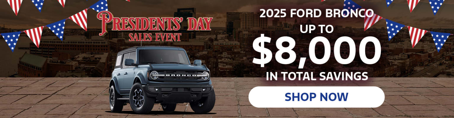 A large gray SUV is displayed in the foreground, with a promotional advertisement for a Presidents' Day sales event in the background, featuring details about savings on a future model.