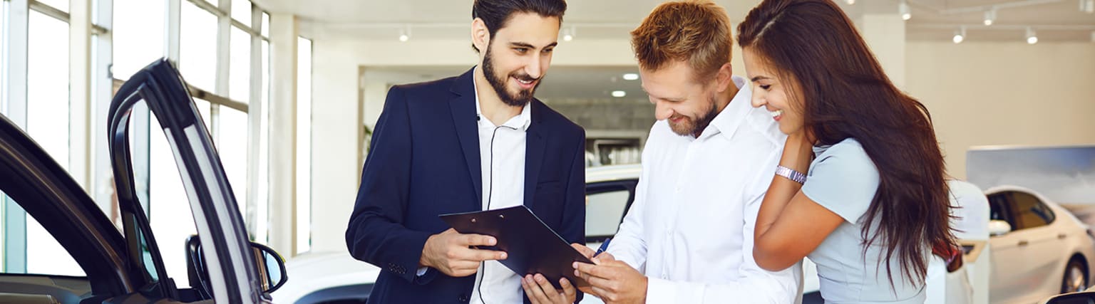 Three individuals, two men and one woman, having a conversation in a professional environment, with one man holding a tablet or clipboard.