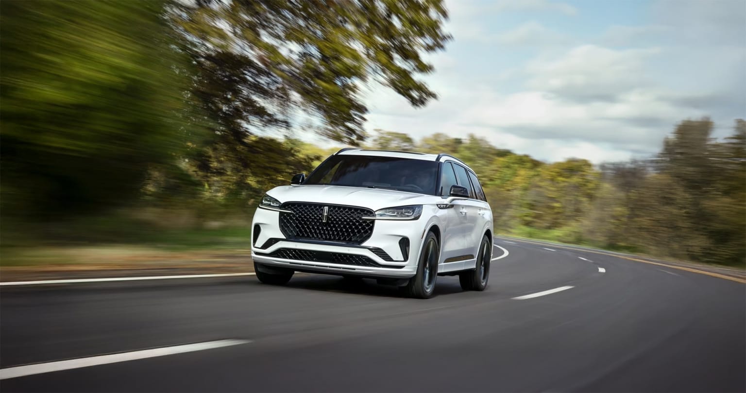 A sleek, white SUV on a winding road surrounded by lush, blurred greenery.