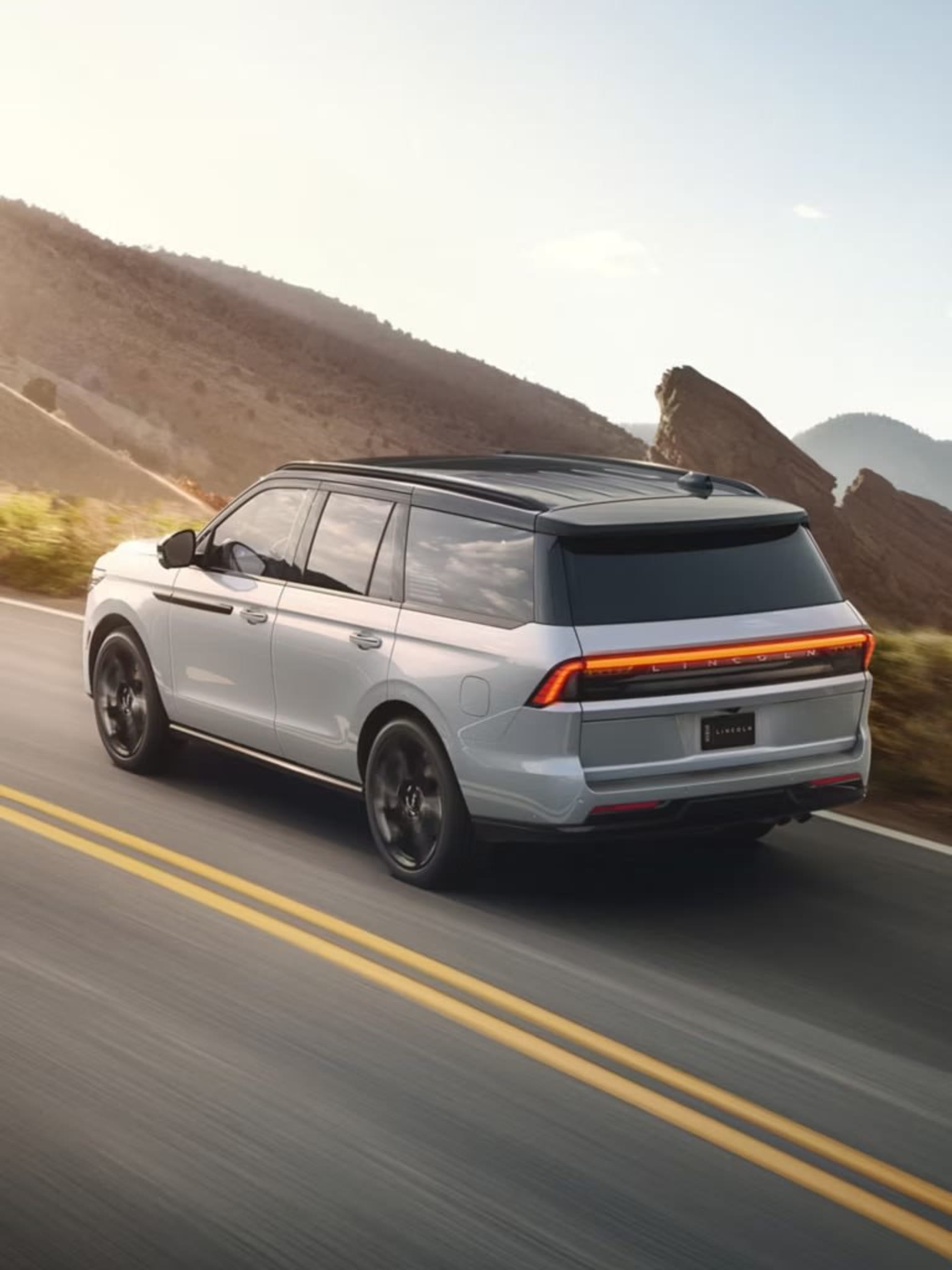 A silver SUV driving on a winding road surrounded by mountainous terrain under a clear sky.
