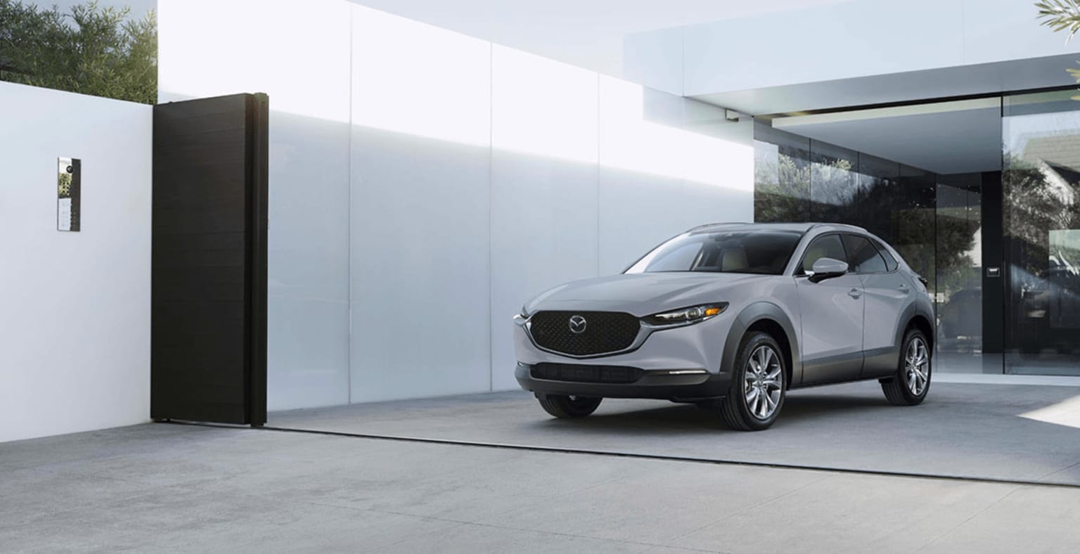 White SUV parked in front of modern building with glass walls surrounded by greenery