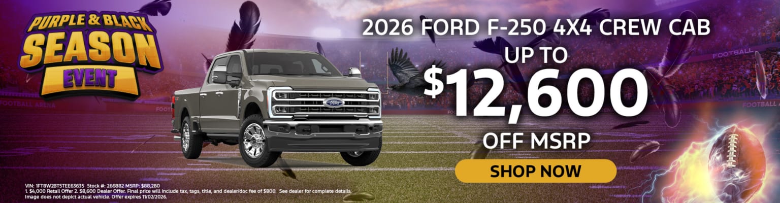 Silver truck parked on football field with background of crowded stadium and event promotion.