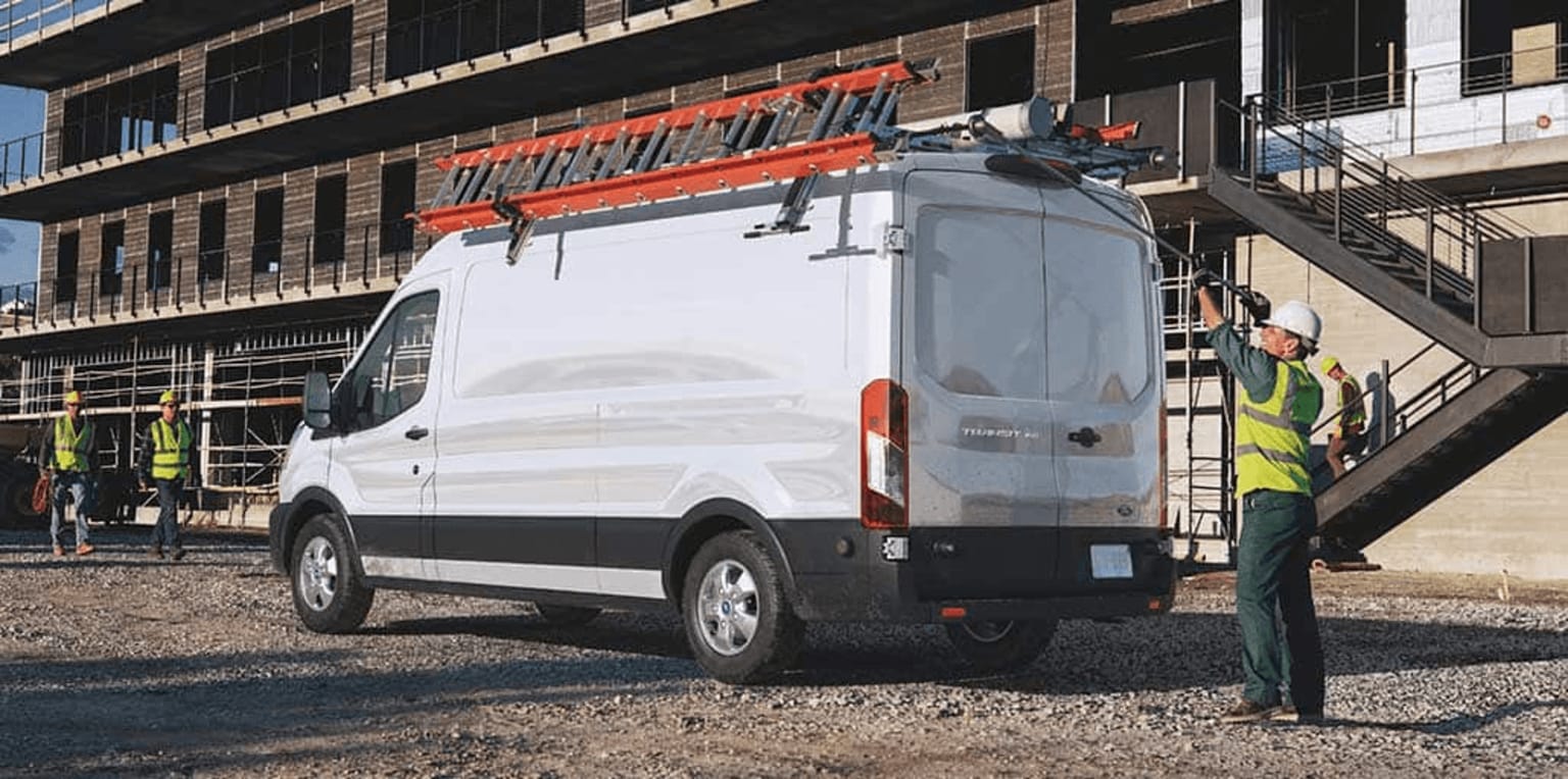 a man standing next to a white van in front of a building with a crane on top of it