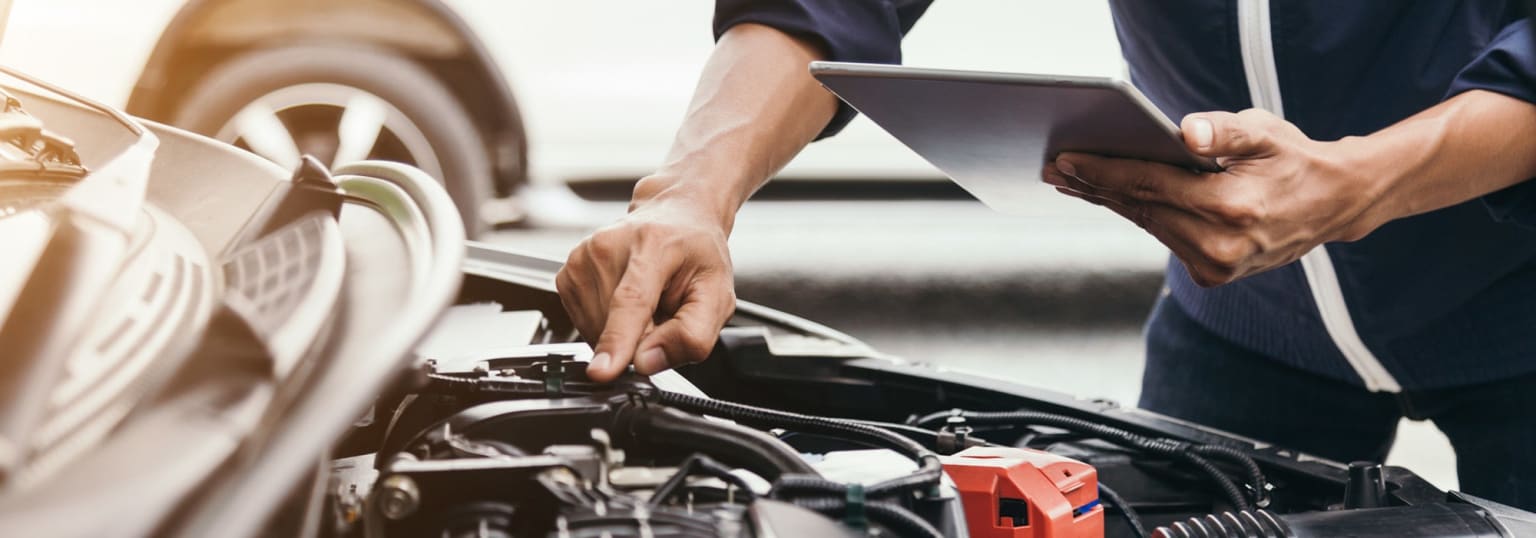 A mechanic's hands working on a car engine, with a mobile device in the background.