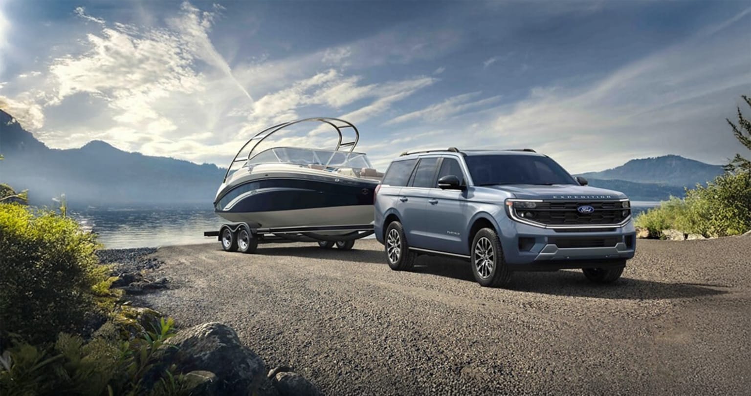 Large white SUV with a boat trailer parked on a dirt road in a scenic natural setting.