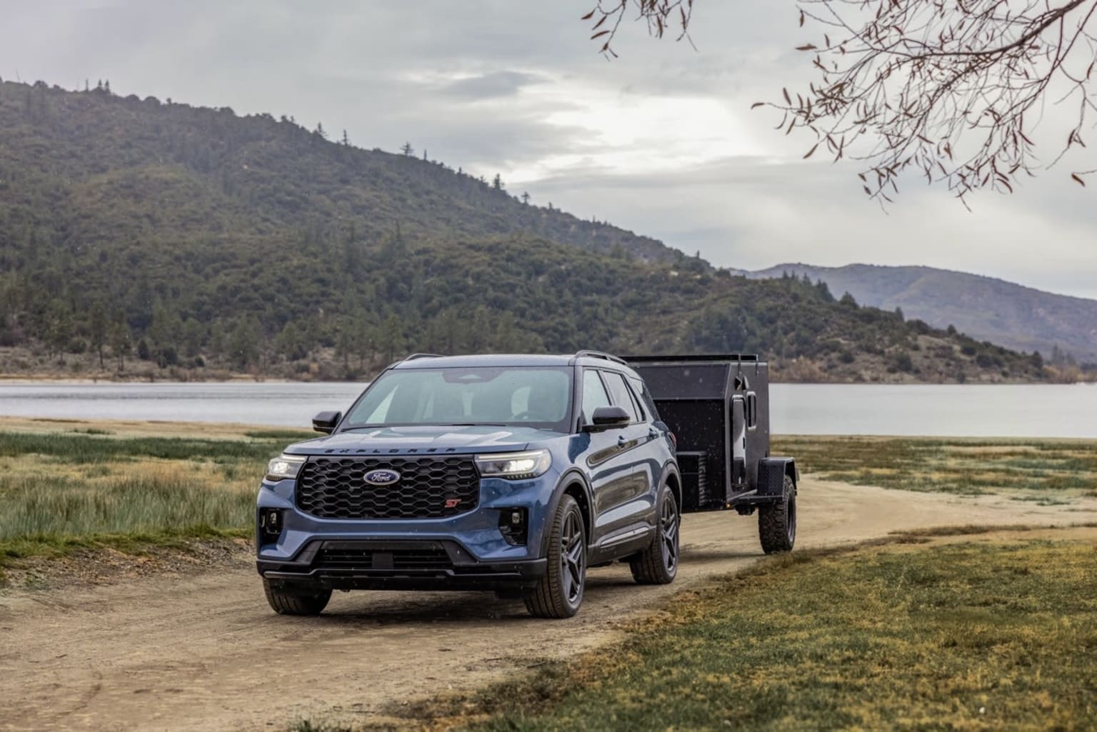 A rugged black pickup truck with a dump bed attachment parked on a grassy field, surrounded by a scenic landscape of mountains and forests.