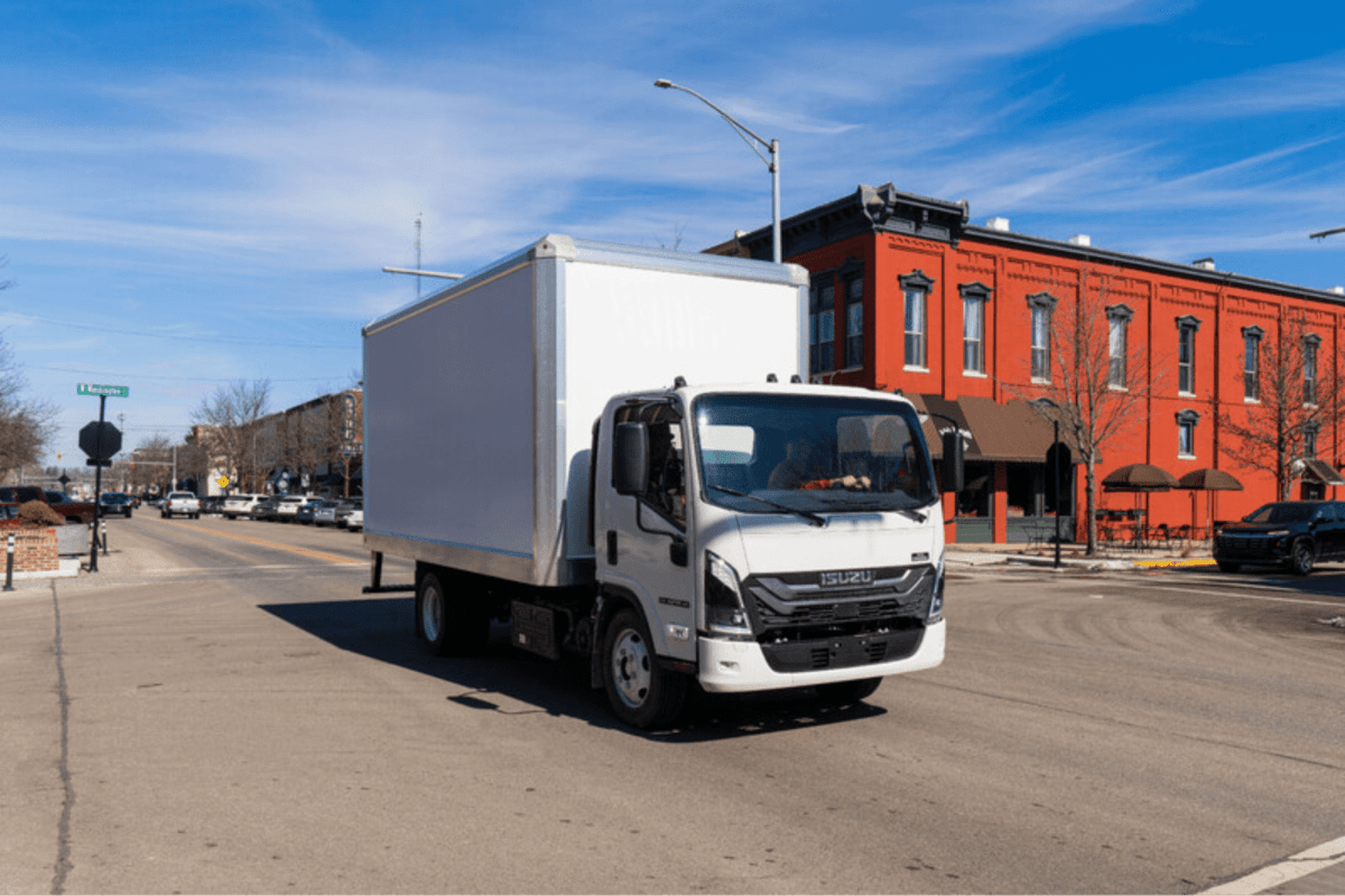 A white box truck parked on a city street in front of a red brick building under a blue sky.