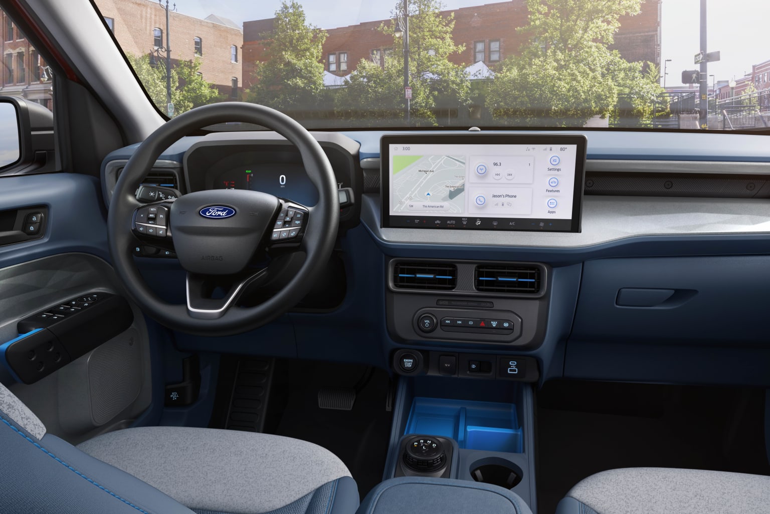 The image shows the interior of a vehicle, with a steering wheel, dashboard, and a large touchscreen display in the center console. The background outside the vehicle appears to be a city street with buildings and trees visible.