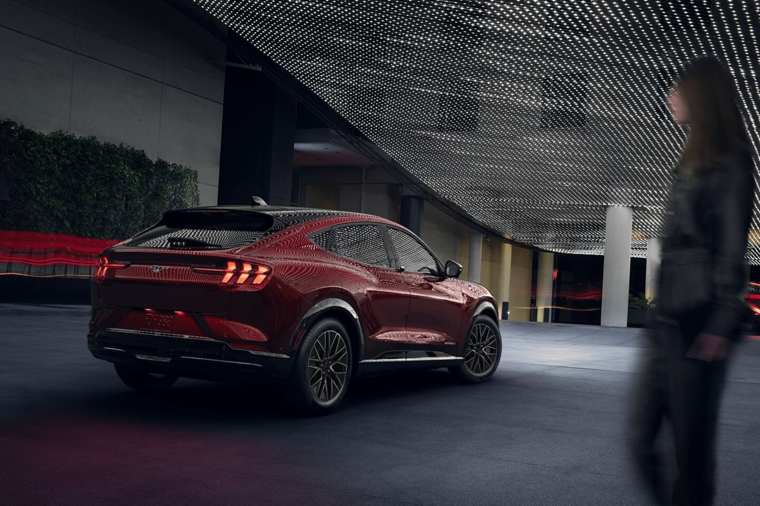 A sleek, red sports car in a dimly lit, modern architectural setting with a mesh-like structure in the background.
