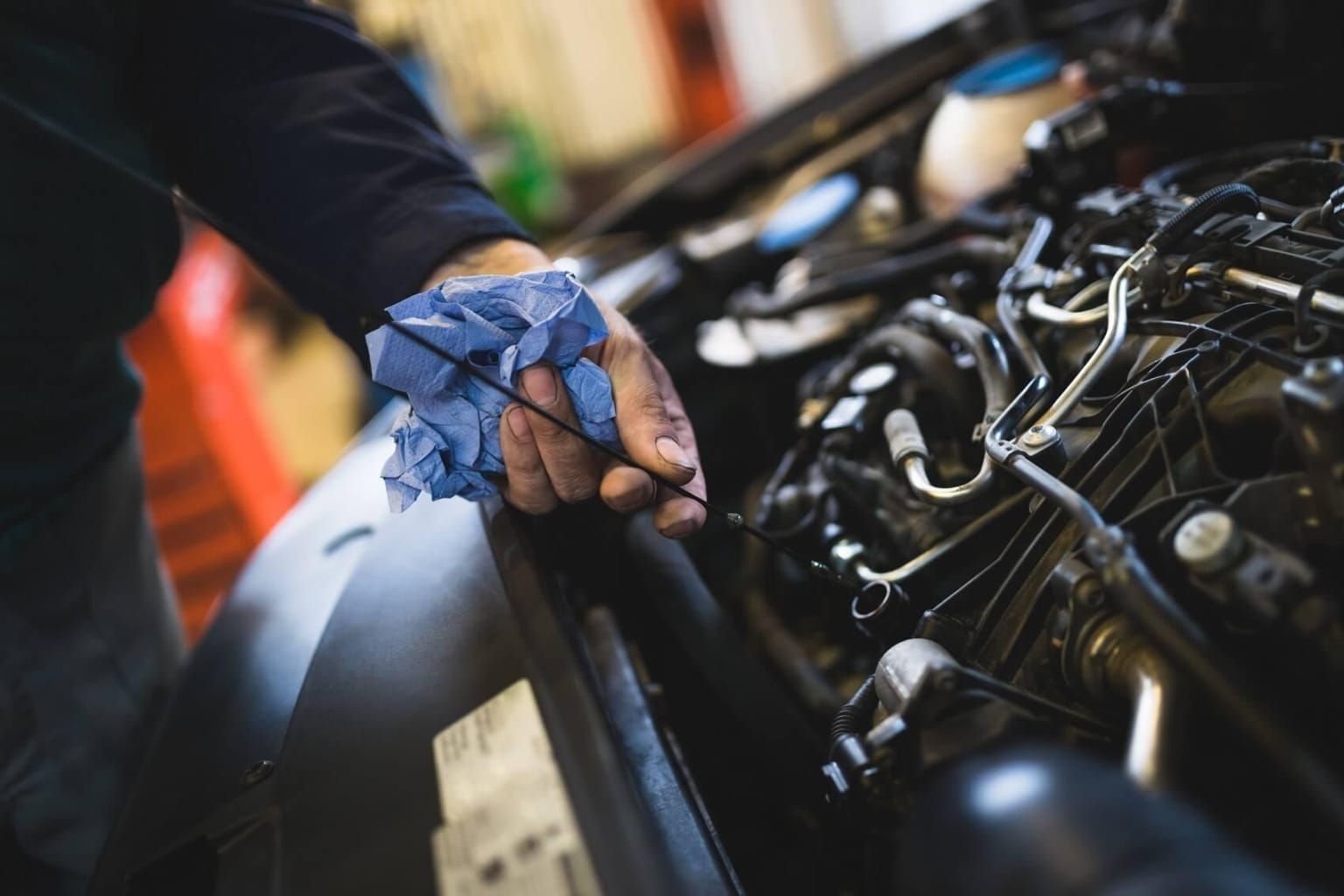 A person's hand, wearing a blue glove, is working on the engine of a motorcycle in a cluttered workshop environment.