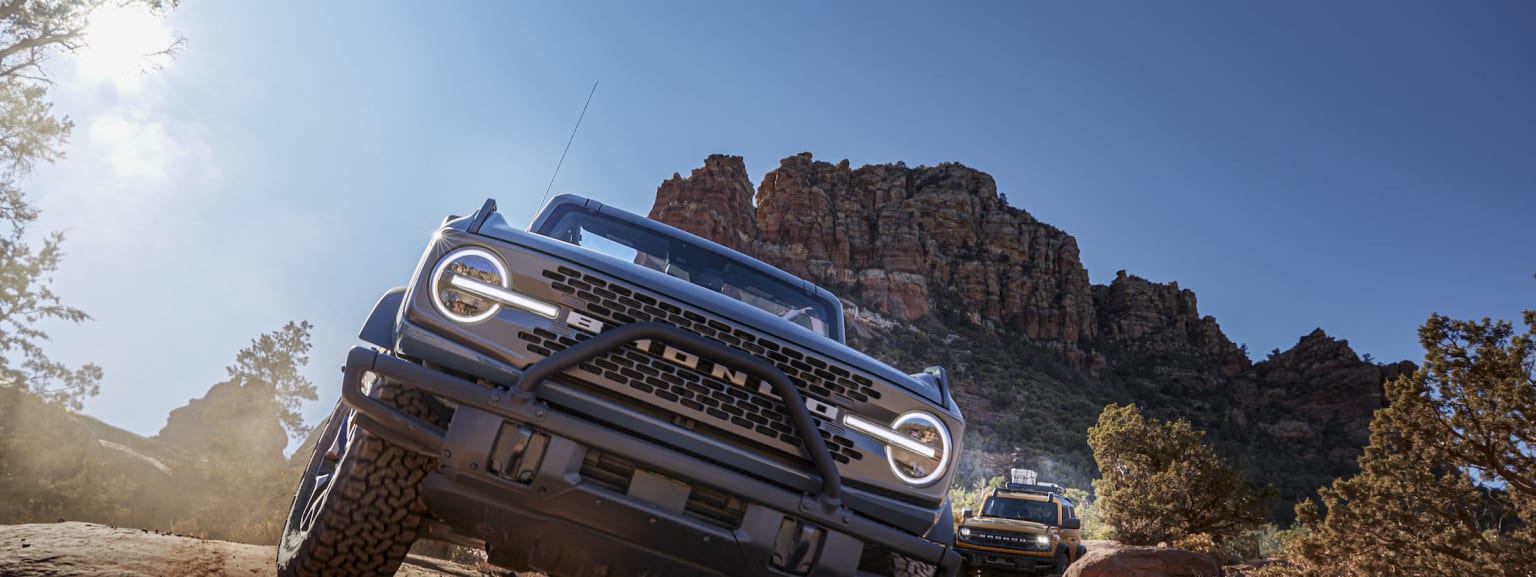 a truck driving down a dirt road in front of a mountain range with a blue sky in the background