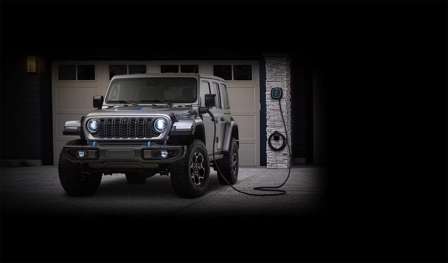 A rugged off-road vehicle parked in a dimly lit garage, its front end illuminated as it charges from an electric charging station.