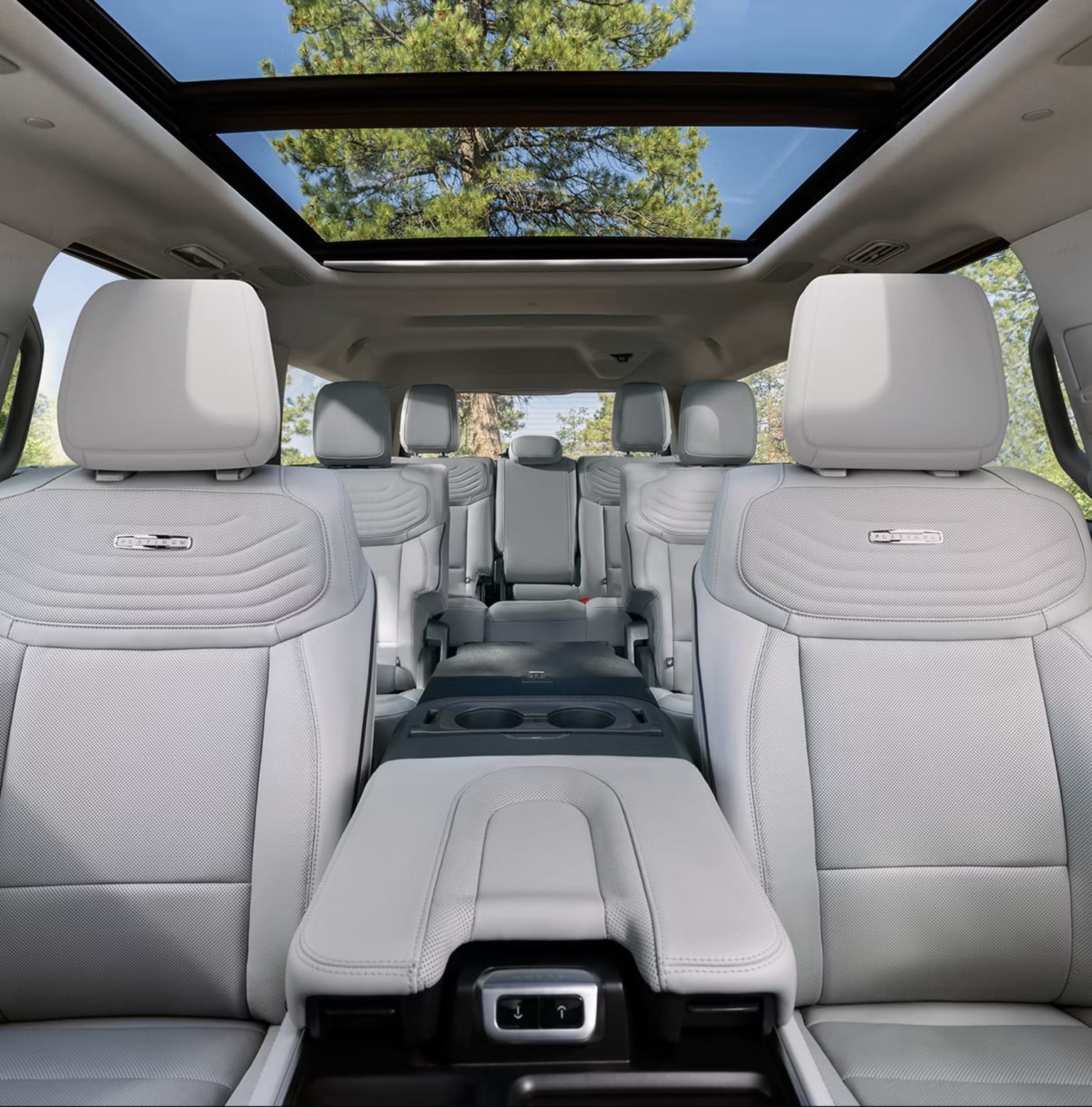 Interior of a spacious vehicle with comfortable-looking seats and a panoramic sunroof providing a view of lush, green trees in the background.