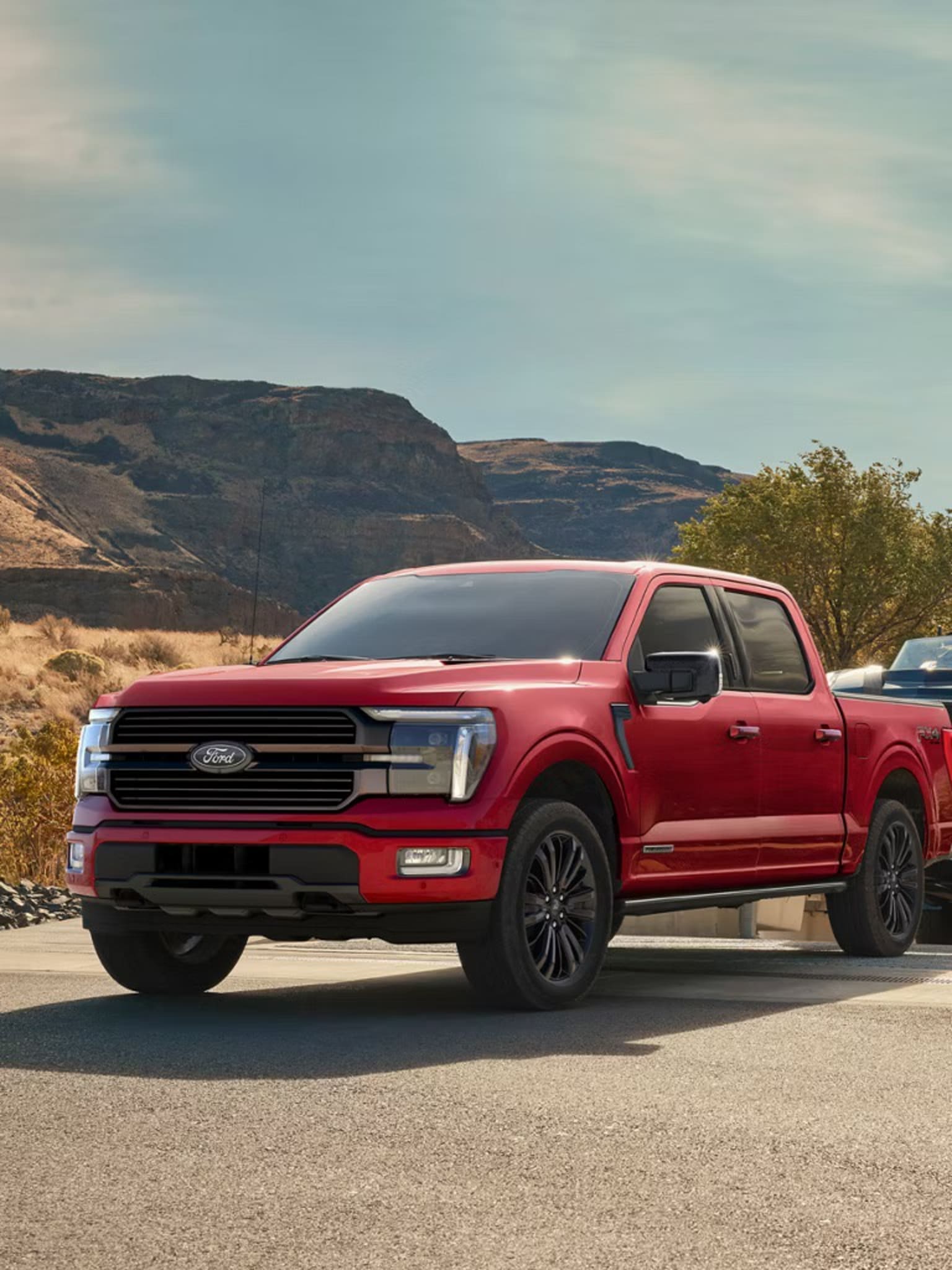 A red pickup truck parked on a road with mountains and clear sky in the background.