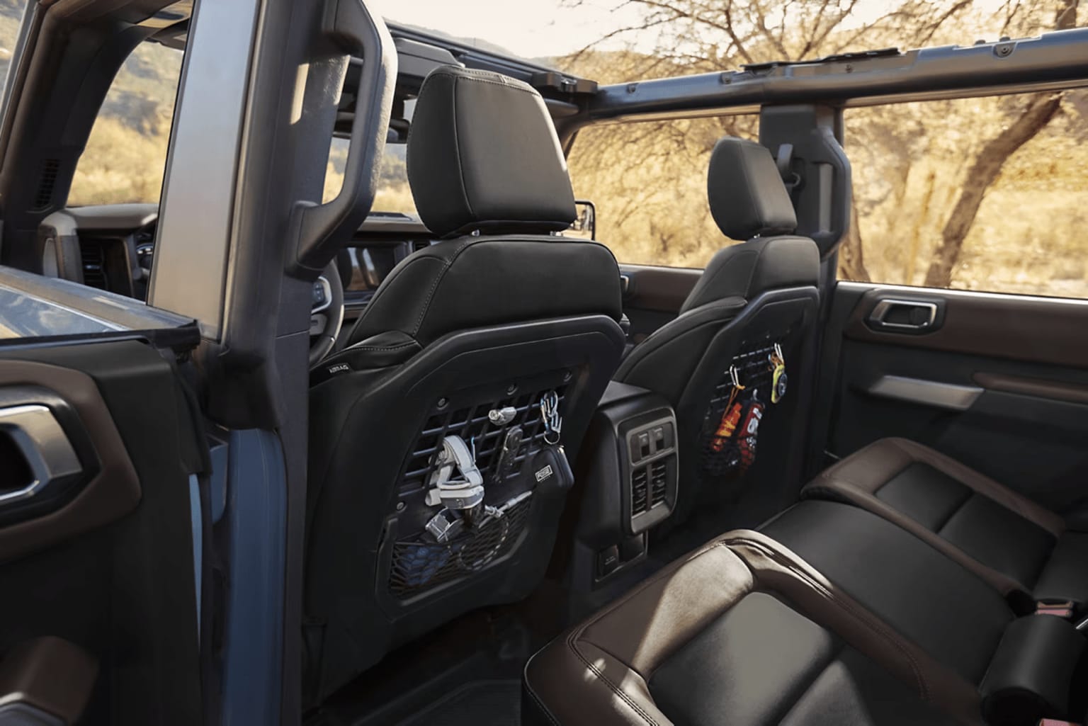Interior of a vehicle with black leather seats, storage compartments, and accessories. Natural outdoor setting visible through the windows.