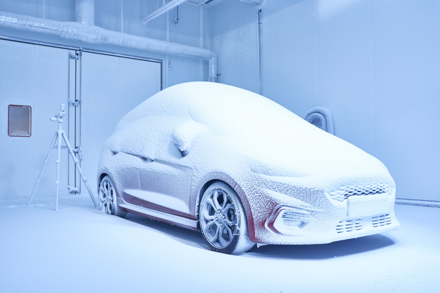 a car covered in snow sitting in a room next to a white wall and a blue light behind it