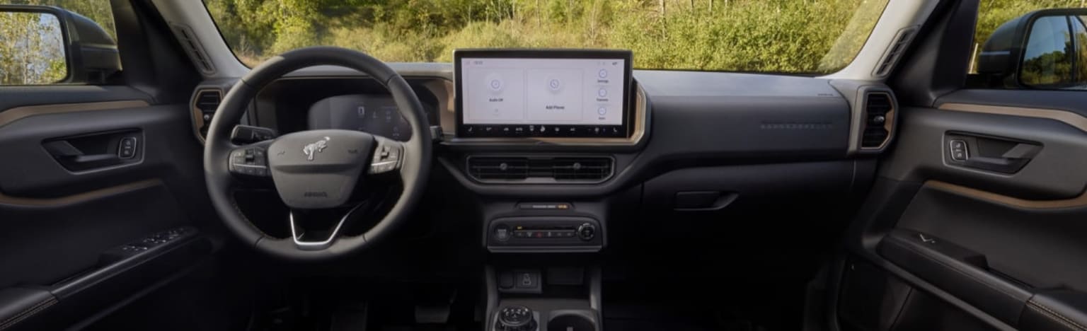 Interior view of a car with a steering wheel and dashboard, with a blurred background of green foliage.
