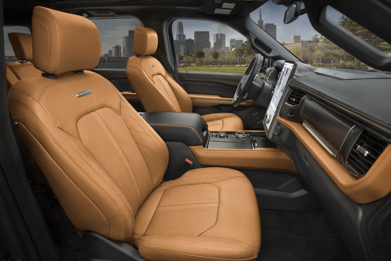 Interior of a luxury vehicle with tan leather seats and a large touchscreen display on the center console, set against a cityscape background with tall buildings.