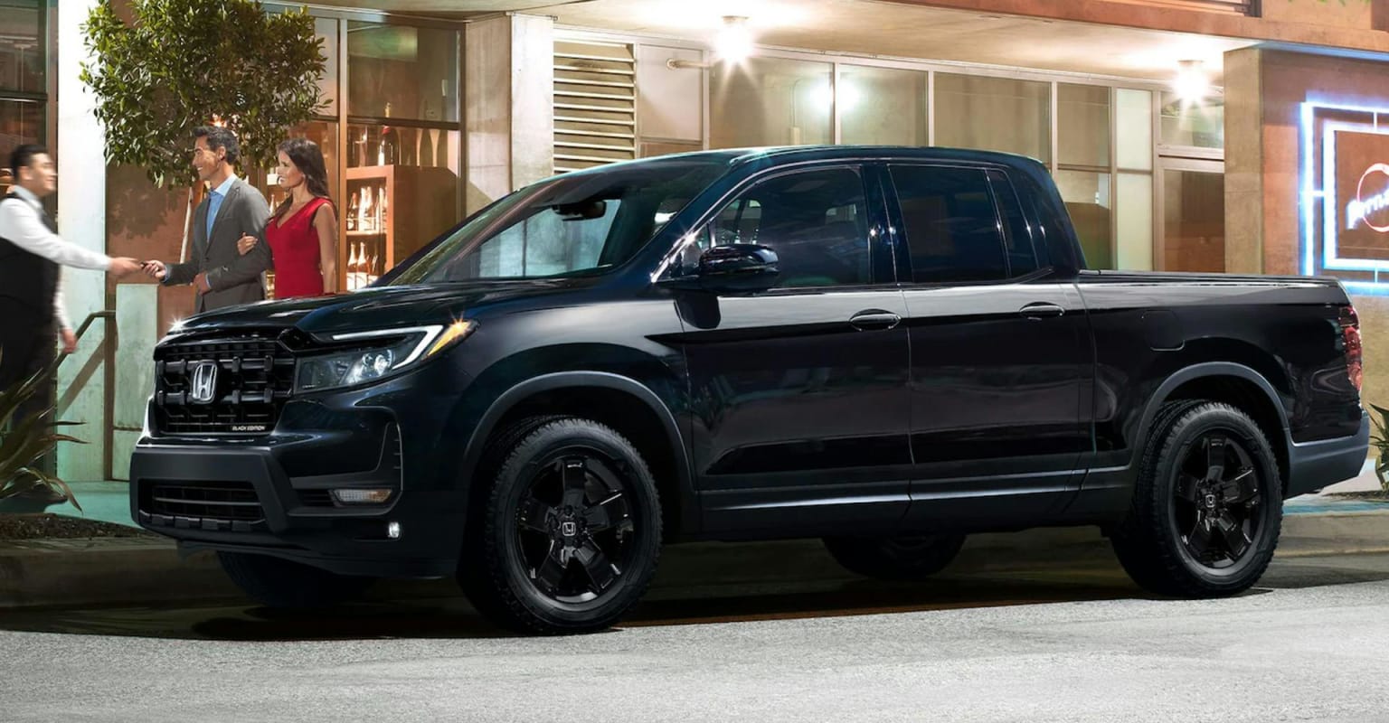 A dark pickup truck parked in front of a building with people in the background.