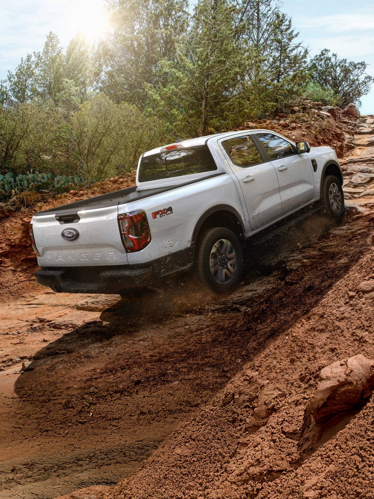 A white pickup truck navigates through rugged terrain surrounded by lush greenery and trees in the background.