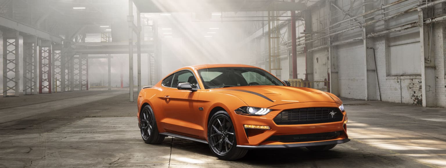 a bright orange mustang mustang car parked in a garage with a bright light shining on it's hood