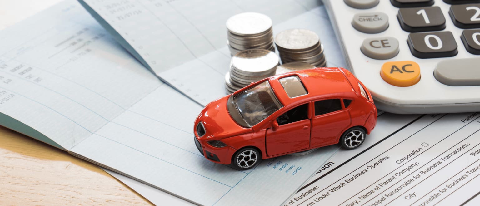 A small red toy car placed on top of financial documents, with a calculator and coins in the background, suggesting a concept related to car financing or automobile-related expenses.