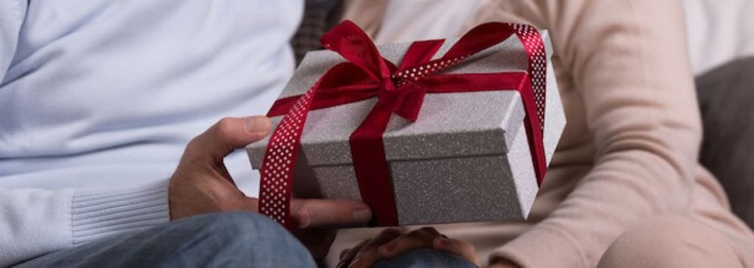 a man holding a wrapped gift box with a red ribbon on it and a woman's arm behind him