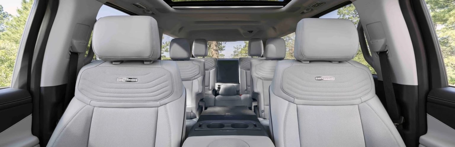 The image displays a vehicle interior with several rows of seats and a sunroof in the background.