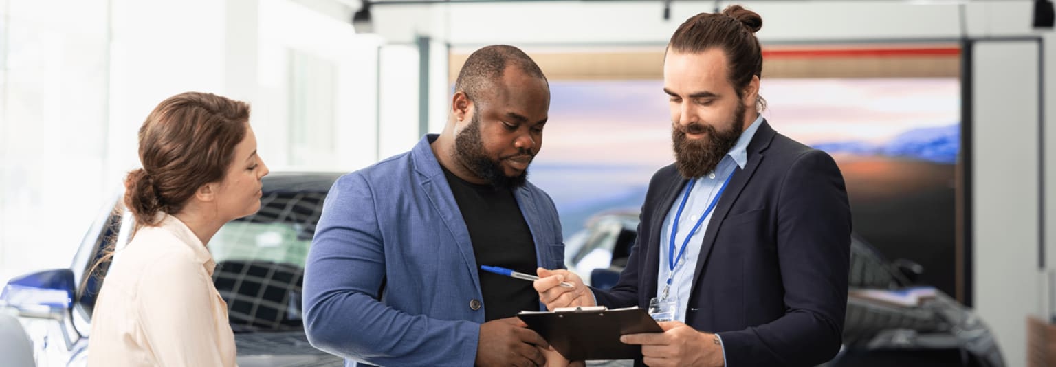 Three individuals, two men and one woman, are engaged in a conversation, with one of the men holding a tablet and the other two appearing to be discussing something.