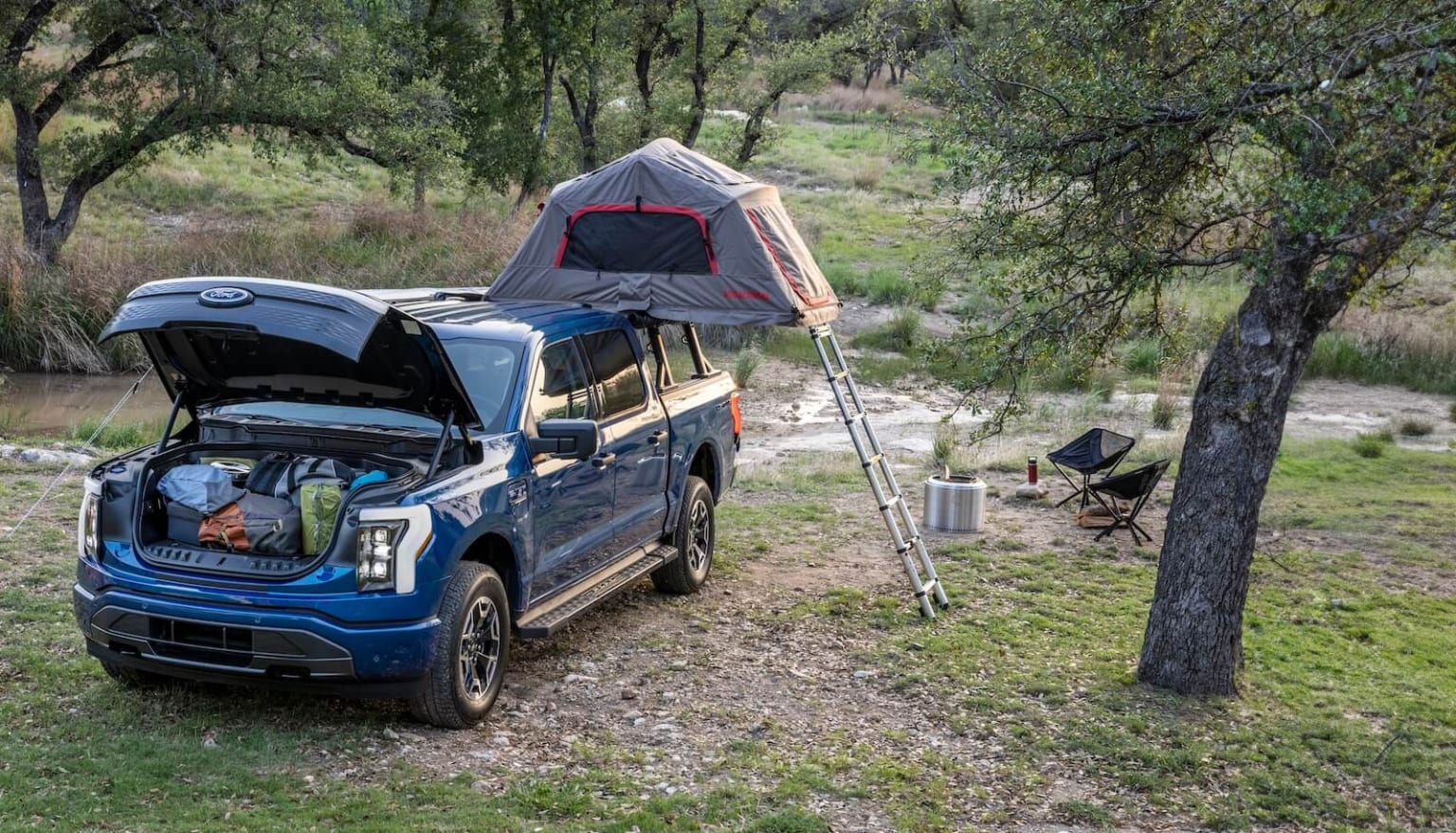 Blue SUV with rooftop tent camping setup in lush, wooded area.