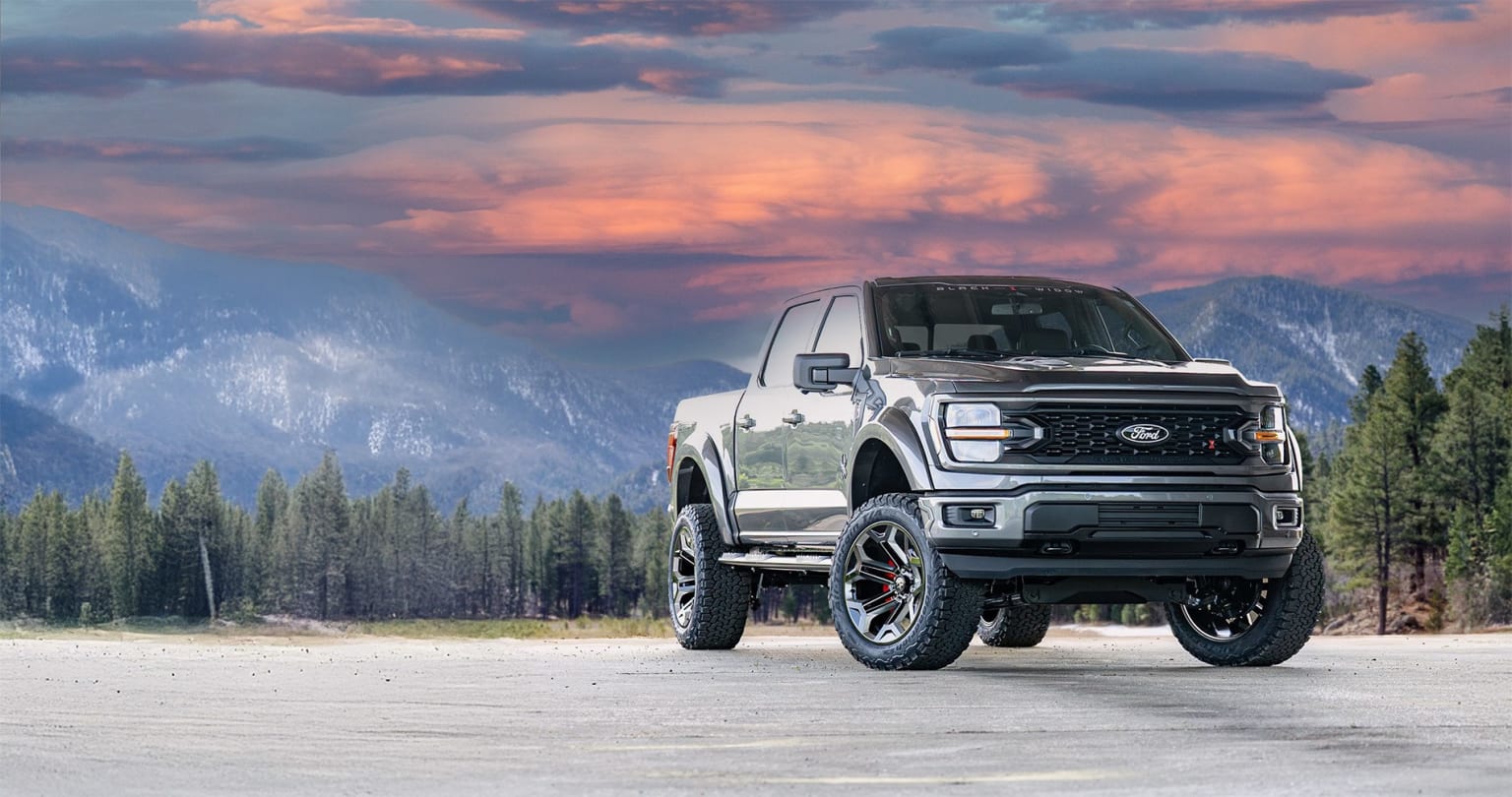 A rugged and powerful pickup truck stands in a snowy, mountainous landscape, with a dramatic sky of vibrant pink and purple clouds overhead.