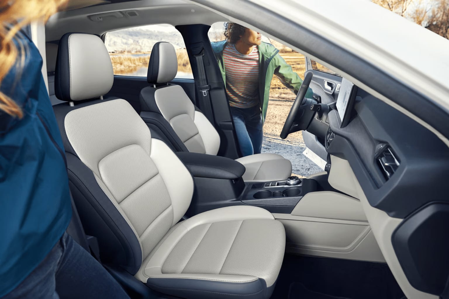The image depicts a vehicle interior with light-colored seats and a person visible in the background through the open door.