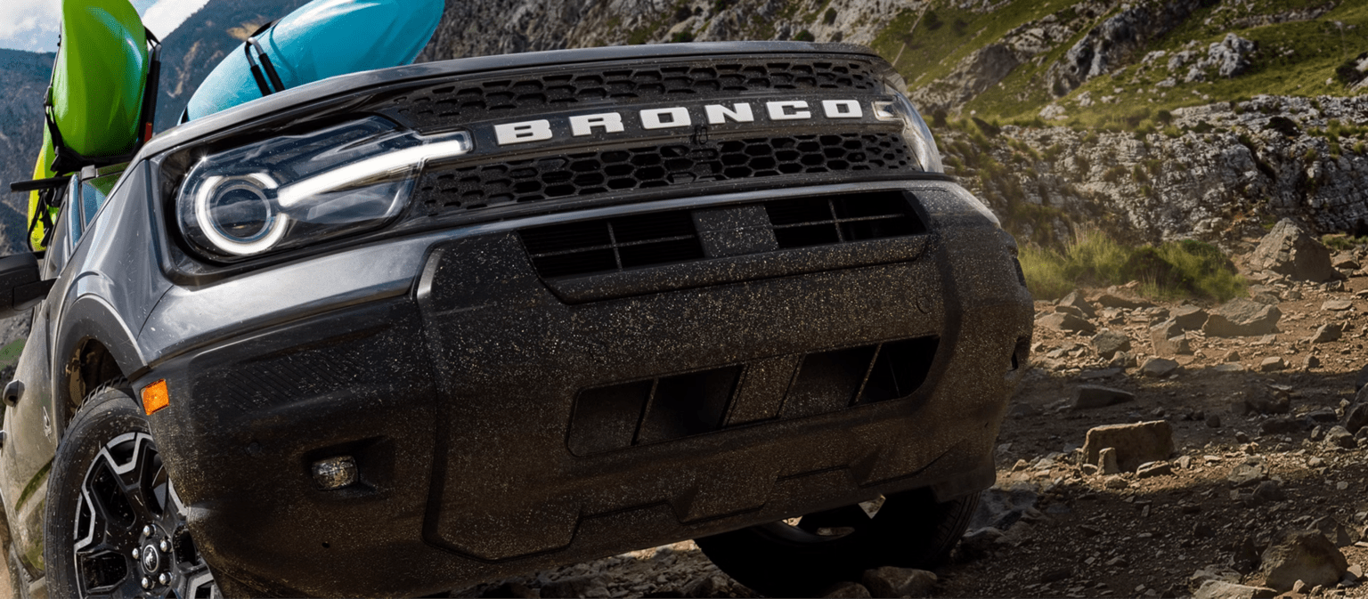 An SUV with kayaks on top drives on a rocky, mountainous terrain.