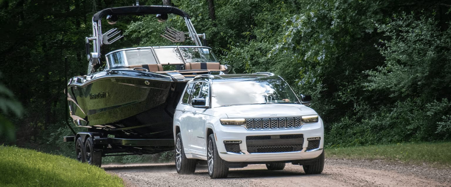 An off-road vehicle towing a boat on a trailer, surrounded by lush green foliage in the background.