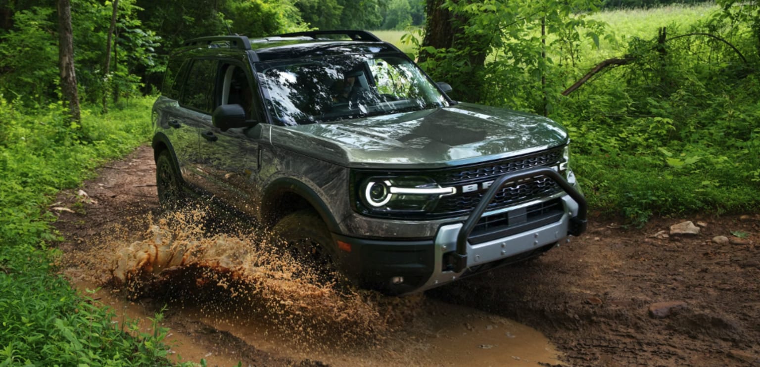 Off-road vehicle driving through muddy forest terrain.