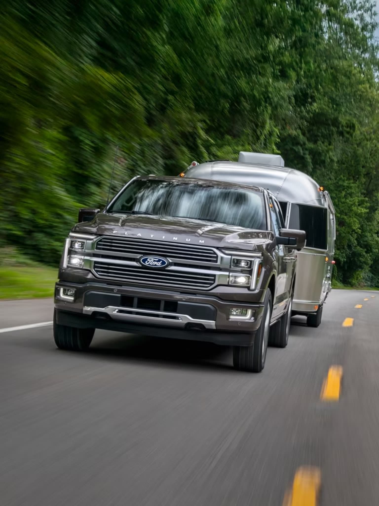 A large, silver SUV is speeding down a winding, tree-lined road, with the surrounding greenery blurred in the background, creating a sense of motion and speed.