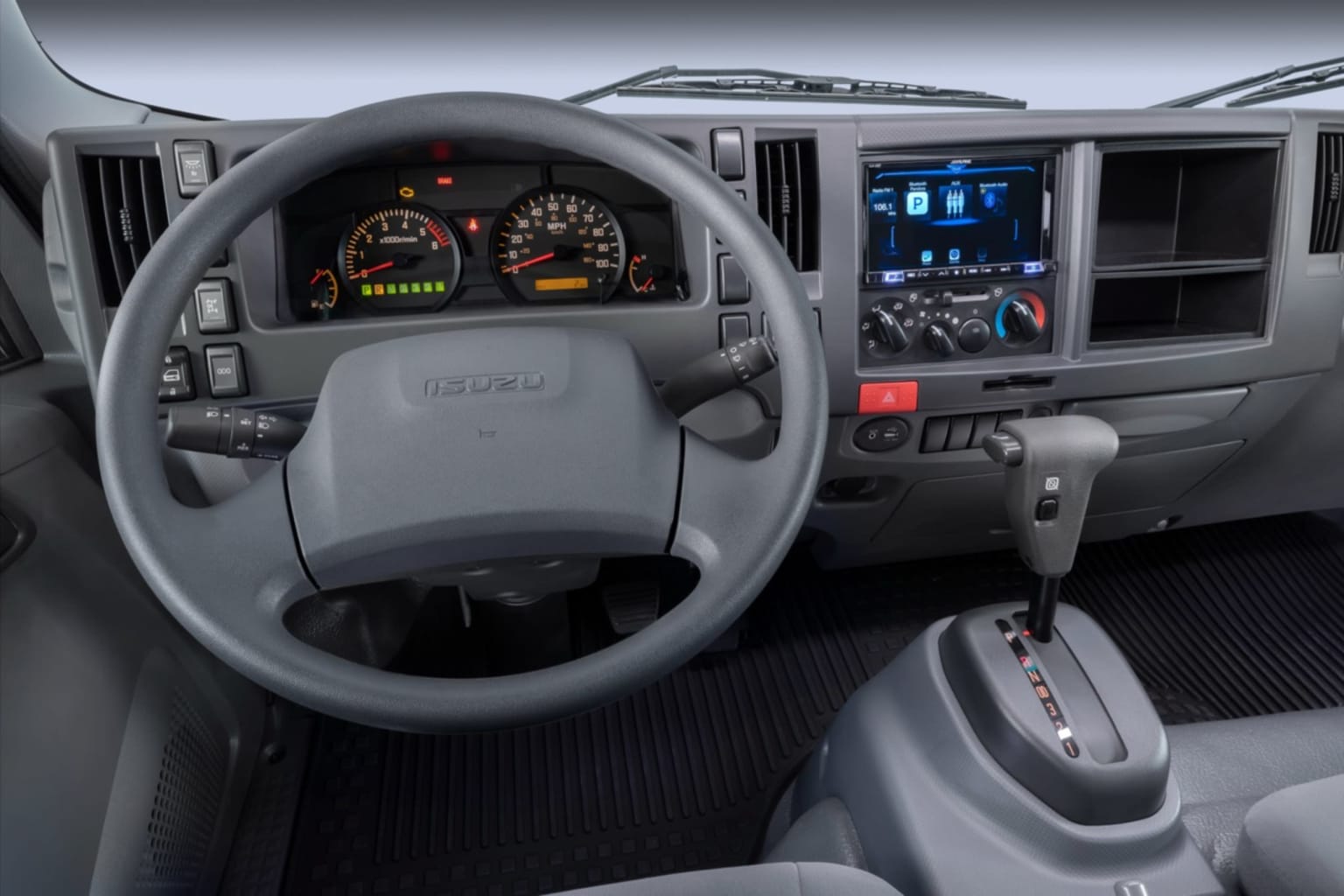 Gray steering wheel and dashboard with a touchscreen infotainment system in the foreground, with the interior of a truck cab visible in the background.