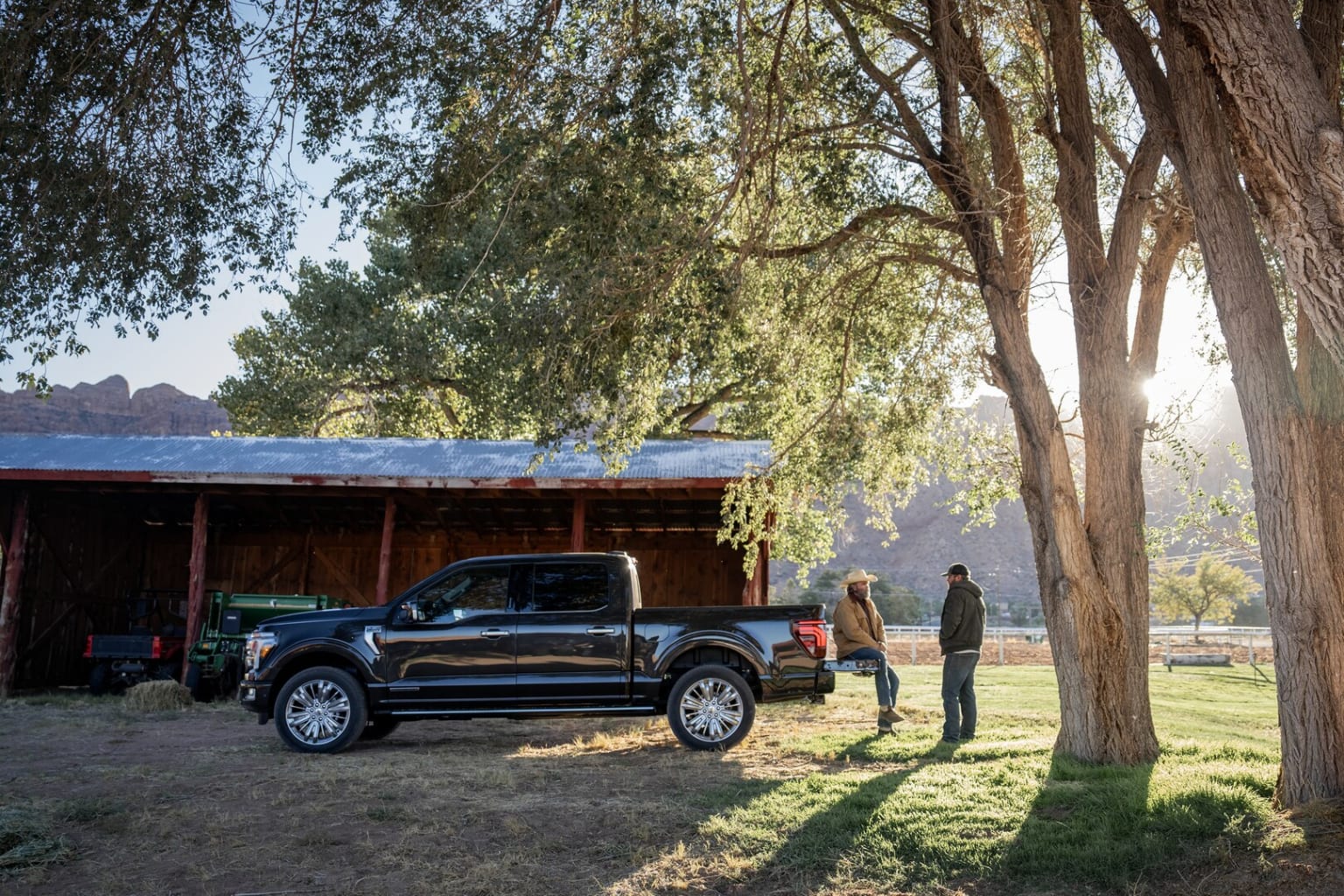 A black pickup truck parked in front of a wooden structure, surrounded by lush greenery and tall trees in the background.