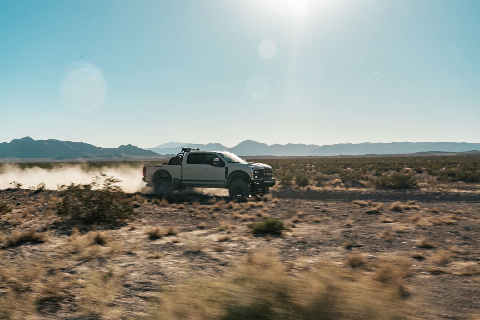 Off-road vehicle in desert landscape with mountains and bright sky