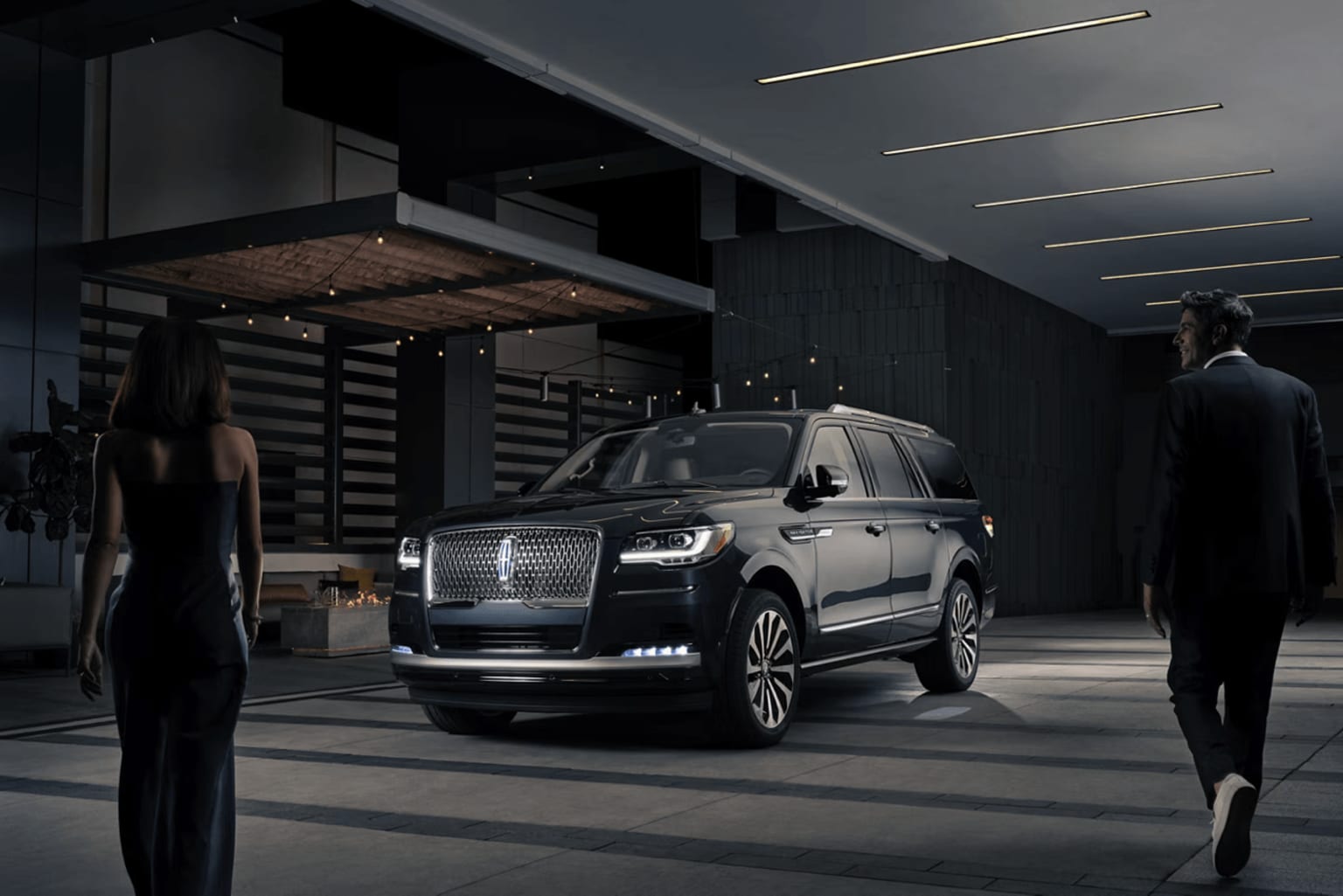 Luxurious SUV in a dimly lit, industrial-style garage with two silhouetted figures.