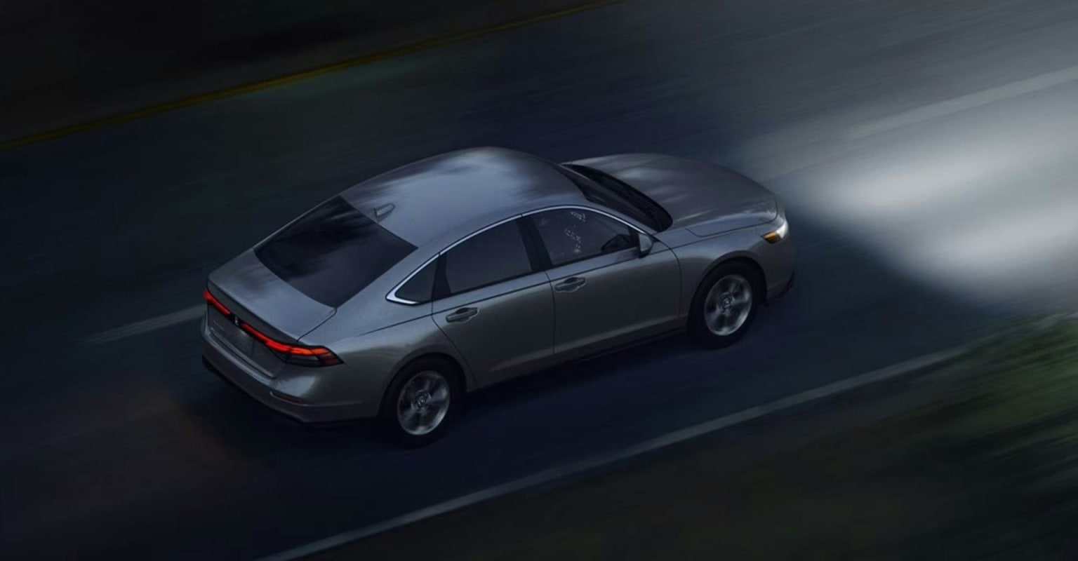 A silver sedan driving on a dark road at night with headlights on.