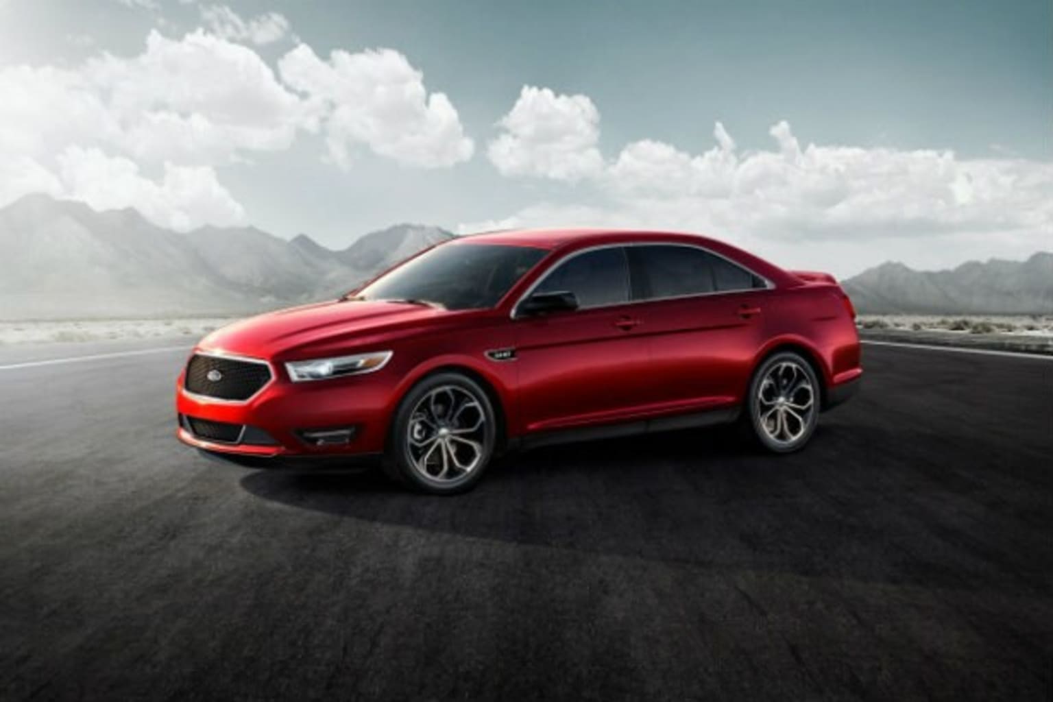 a red car driving down a road with mountains in the background and clouds in the sky in the background