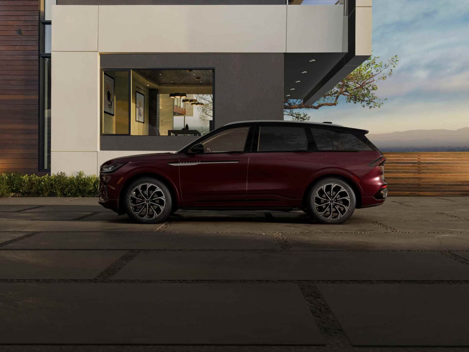 A burgundy-colored SUV parked in front of a modern, minimalist building with a glass facade and landscaping elements.