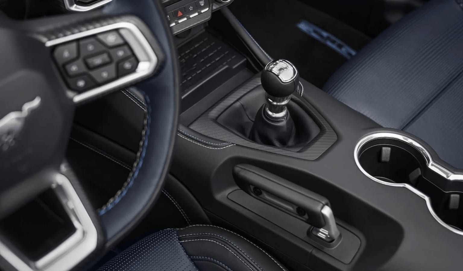 The image displays the interior of a vehicle featuring a gear shift, various controls, and a dark, textured surface in the foreground.